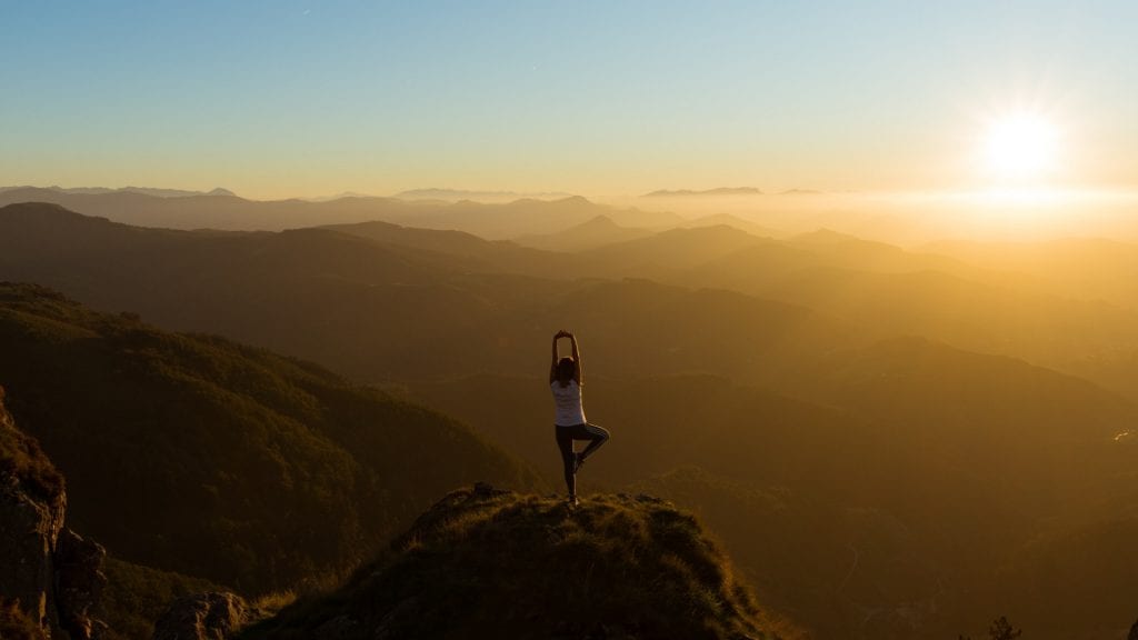 A person doing yoga on a mountain at sunset