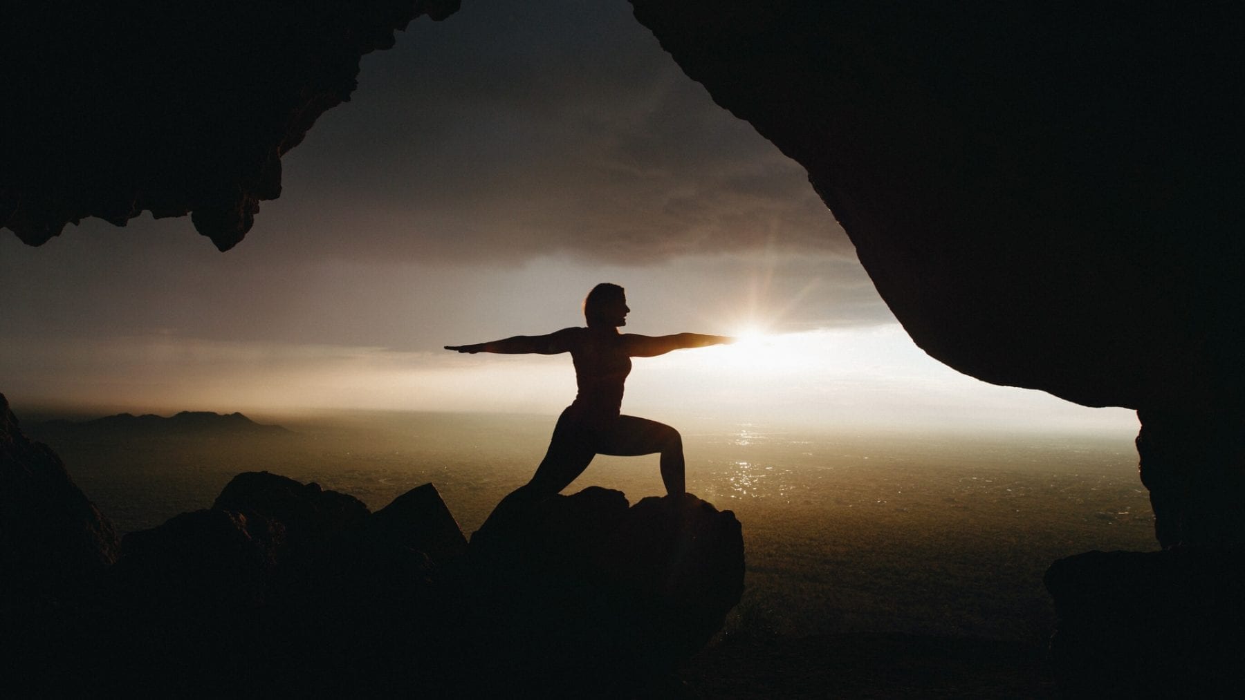 A person doing yoga on a cliff at sunrise